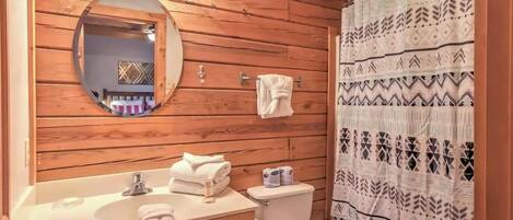 A wooden cabin bathroom with a round mirror, a sink, a toilet, and a shower curtain.
