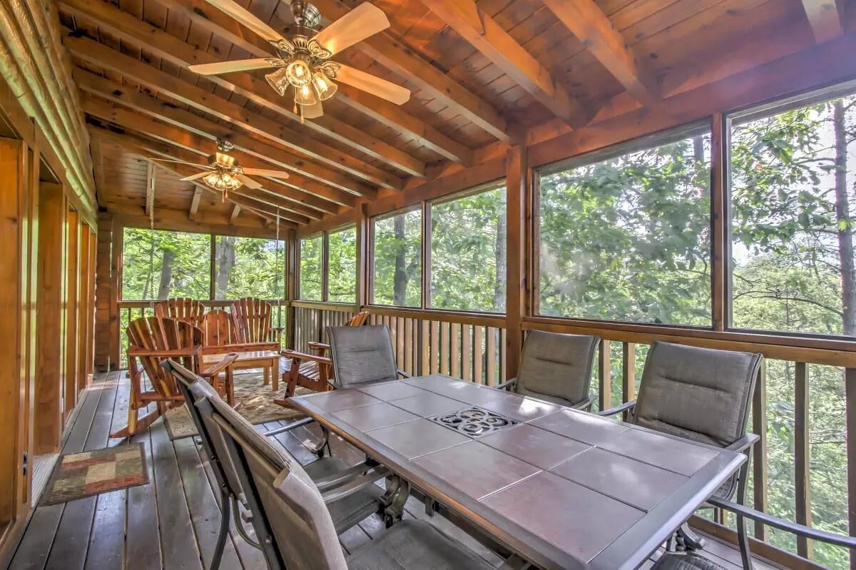A wooden deck with a table and chairs, large windows, and ceiling fans.