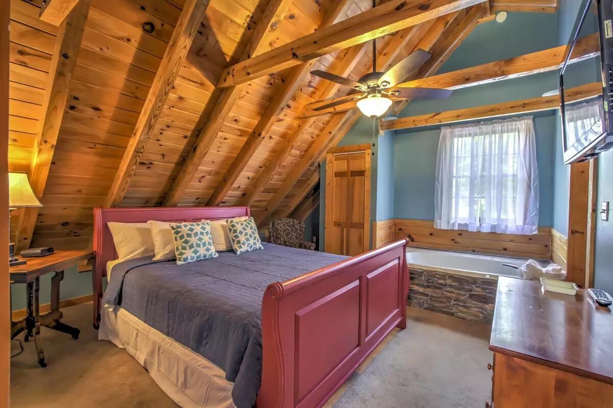 Une chambre à coucher avec un plafond en bois, un lit, un bureau et une fenêtre avec des rideaux.