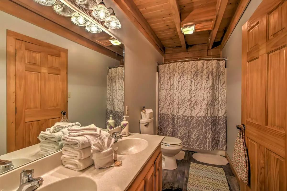A bathroom with wooden beams, a sink, a toilet, and a shower curtain with a tree pattern.