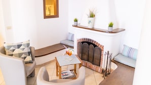 A living room with a fireplace, a sofa, a chair, and a small table with a magazine. - Goat Path (Positano)
