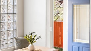 Ein Essbereich mit Tisch, Stühlen, einer Vase mit Grünpflanzen, einem Fenster mit Dekorationsglas und einer blauen Tür.
