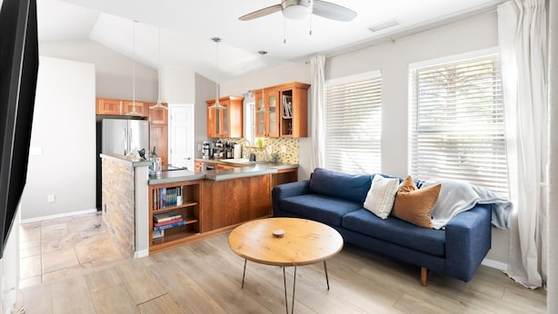 Ein modernes Wohnzimmer mit einem blauen Sofa, einem Holztisch und einer Küchenzeile mit Holzschränken und einem Kühlschrank.