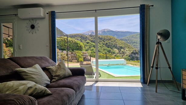 A living room with a sofa, a pool, and a view of mountains.