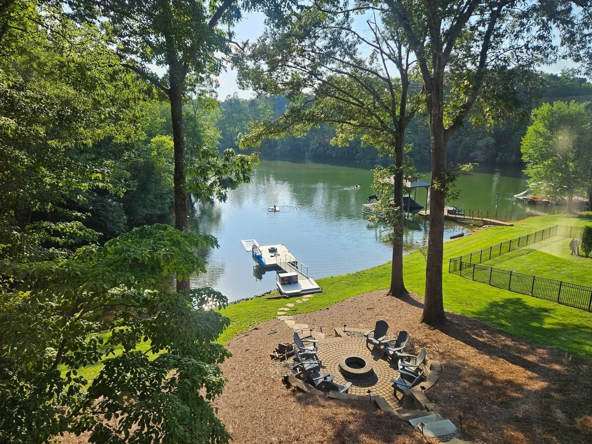 A lakeside view with a dock, chairs, and a fire pit.