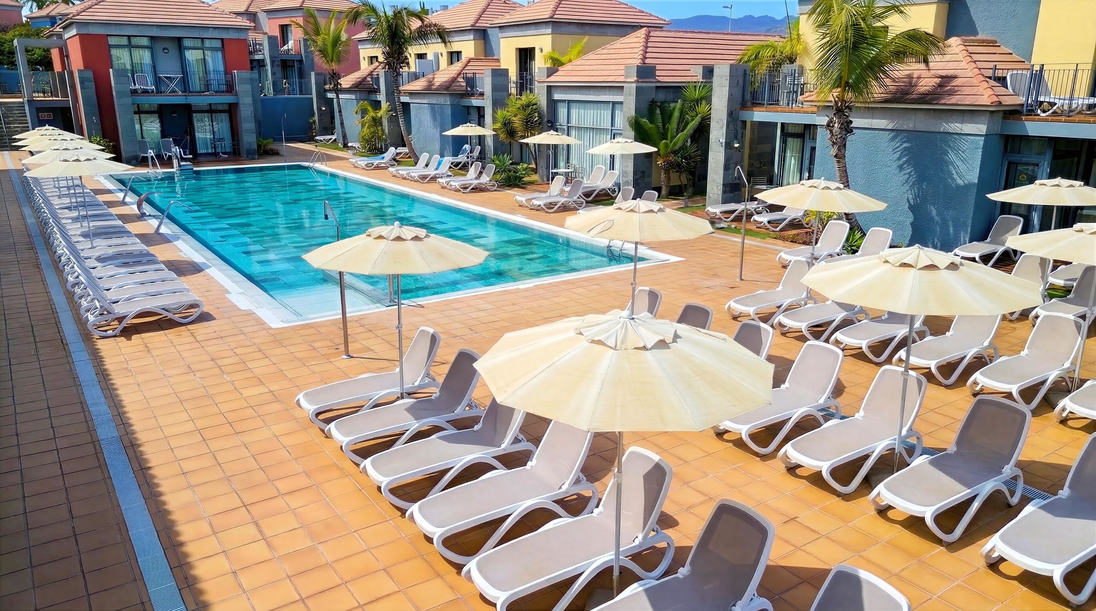 A pool area with sun loungers and umbrellas, surrounded by buildings with balconies.