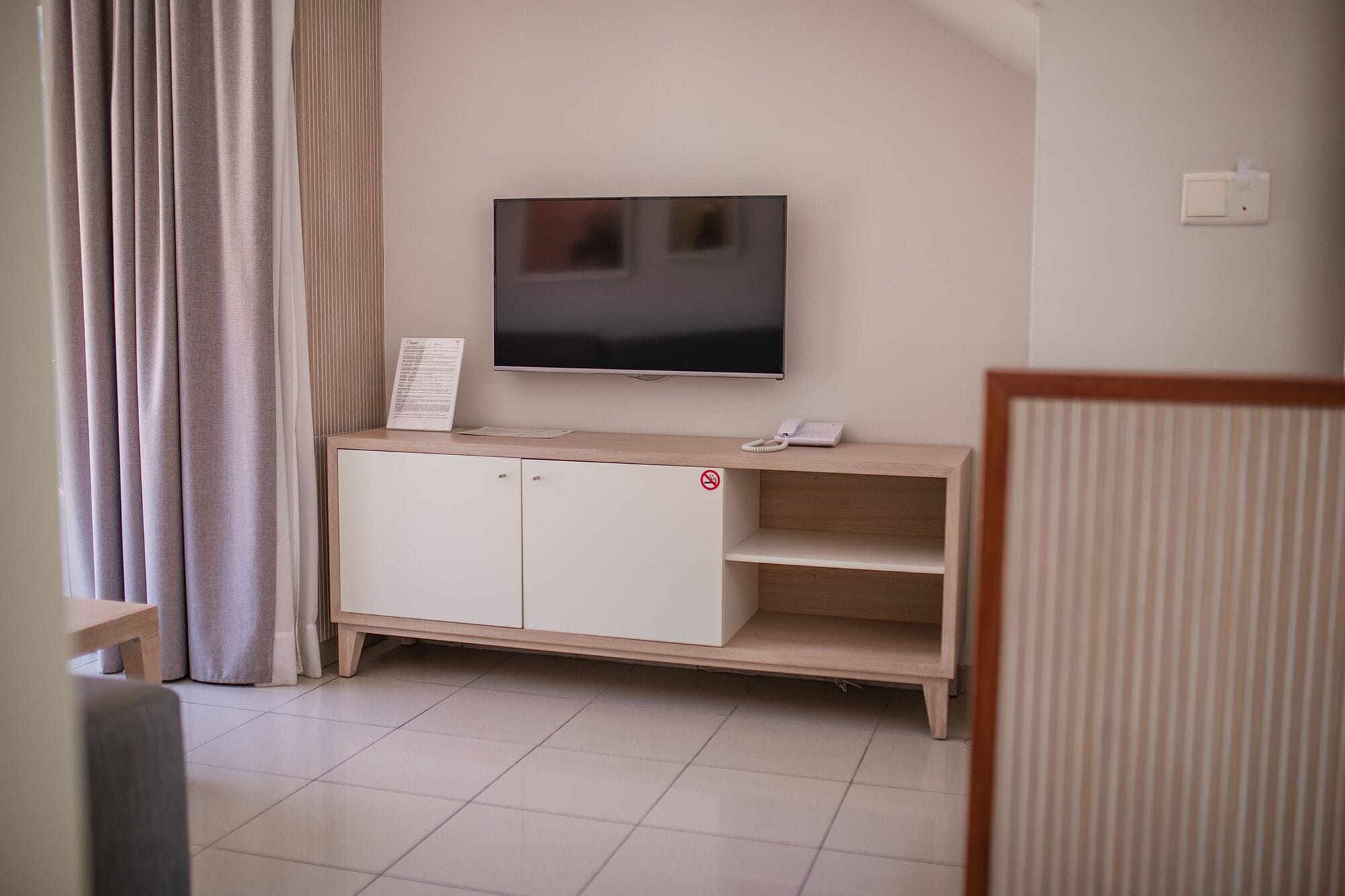 Una sala de estar con un televisor de pantalla plana montado en la pared, un mueble de madera con un letrero de prohibido fumar y un teléfono encima.