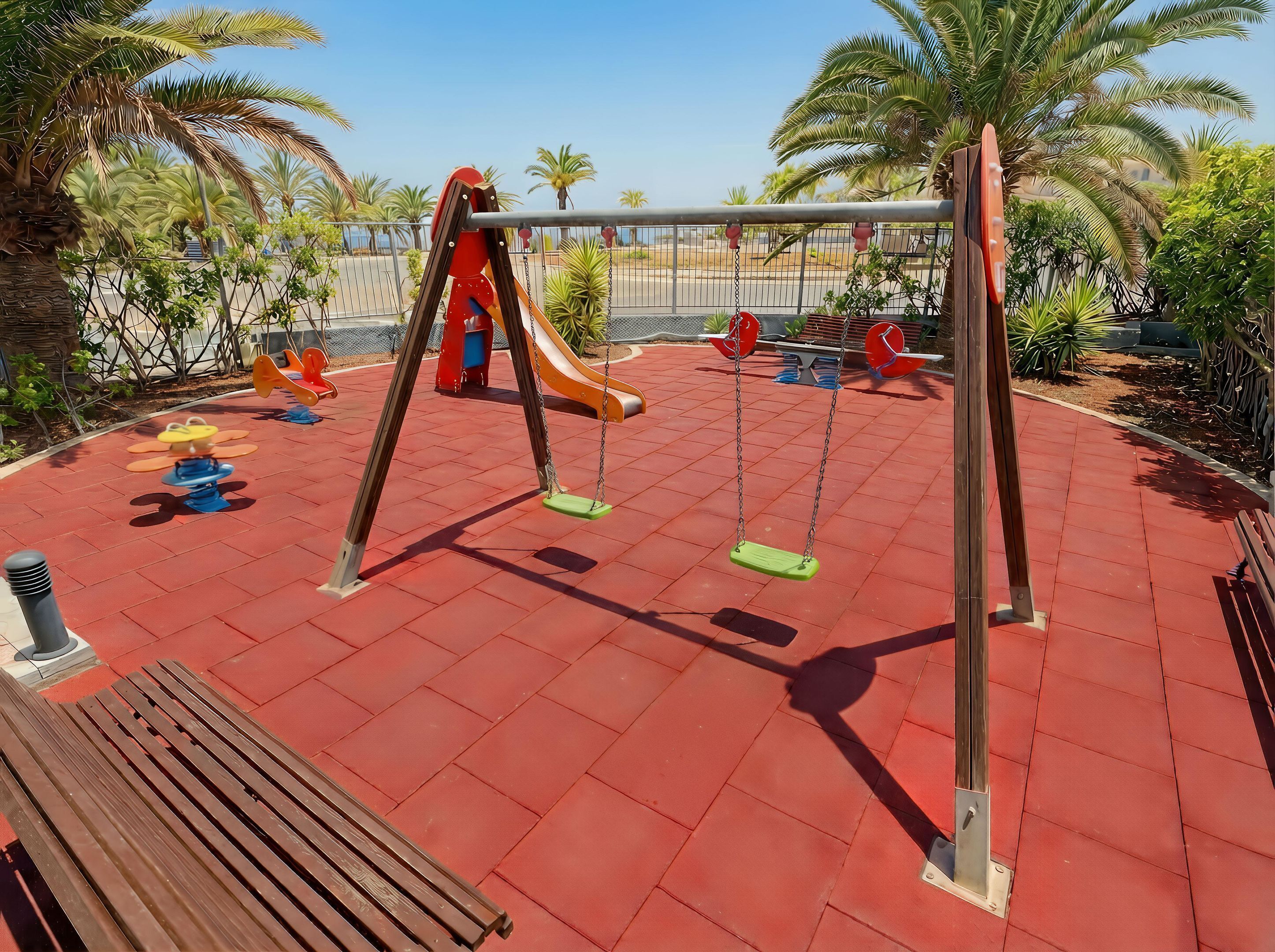 Un parque infantil con columpios, tobogán y un banco.