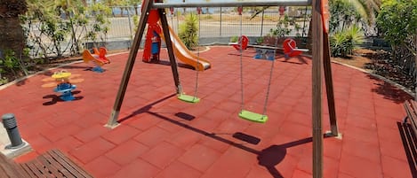 Un parque infantil con columpios, tobogán y un banco.