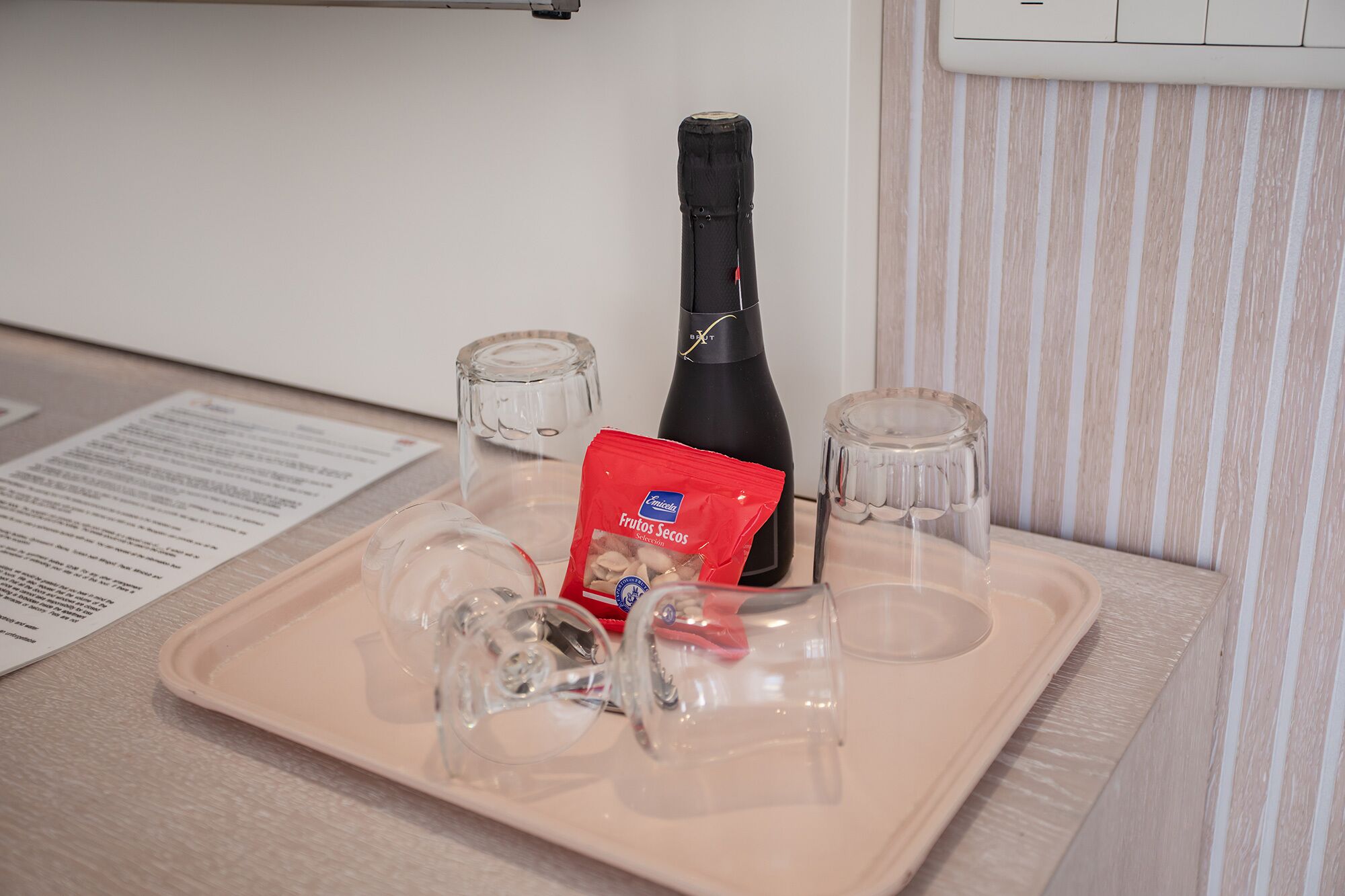Ett bricka med en flaska, ett paket snacks och två glas på ett bord.