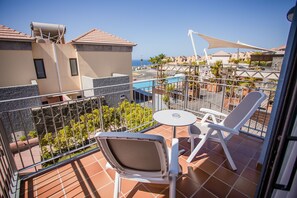 A balcony with a white table and two white chairs, overlooking a swimming pool and neighboring buildings. - Caybeach Meloneras (San Bartolomé de Tirajana)