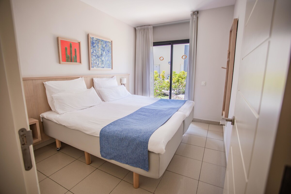 A neatly made bed with a blue throw blanket, a wooden headboard, and two framed artworks on the wall.