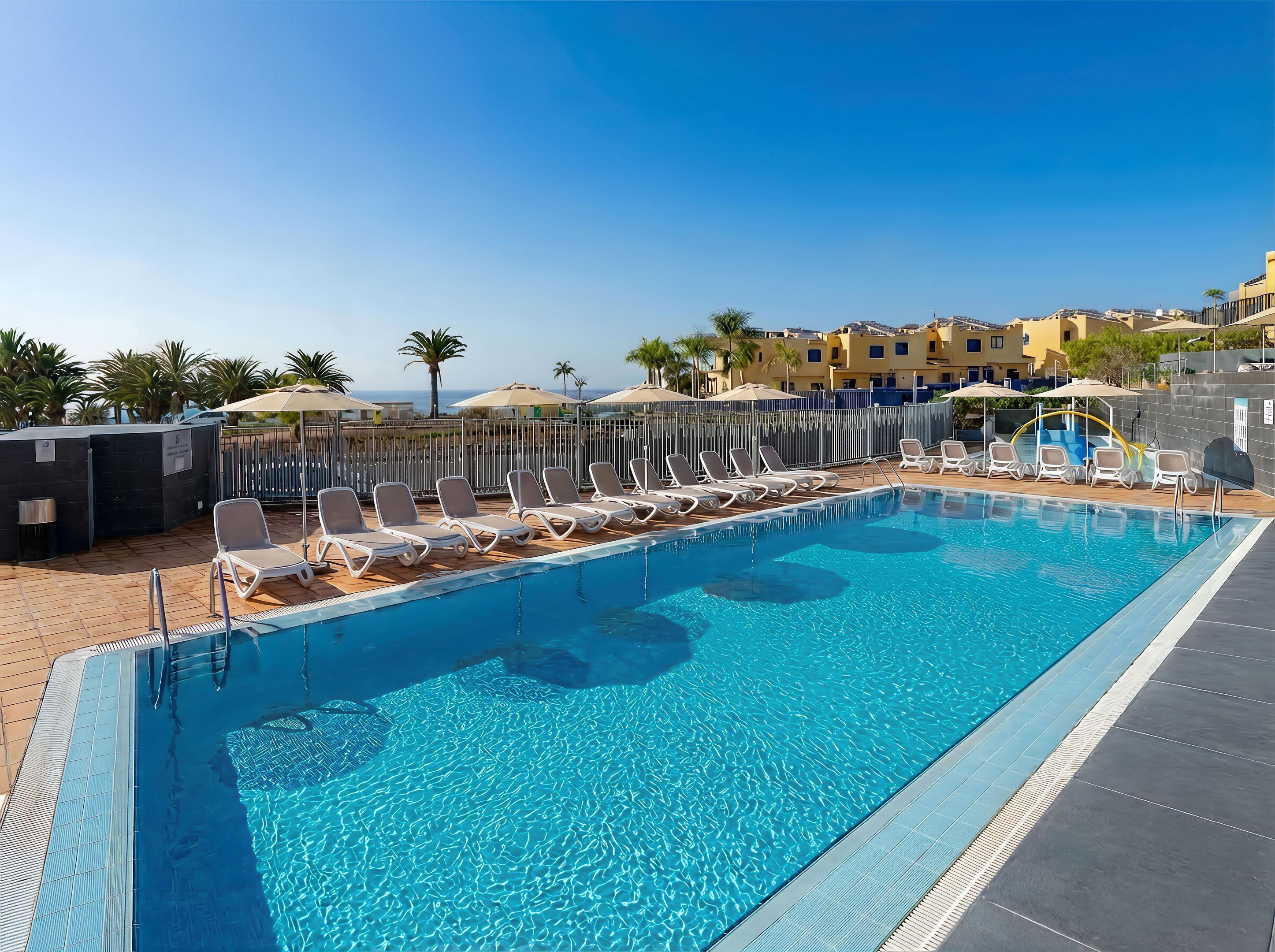 A swimming pool with lounge chairs, a sun umbrella, and a view of buildings in the background.