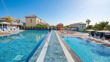A swimming pool with lounge chairs and umbrellas, surrounded by buildings with balconies and palm trees.