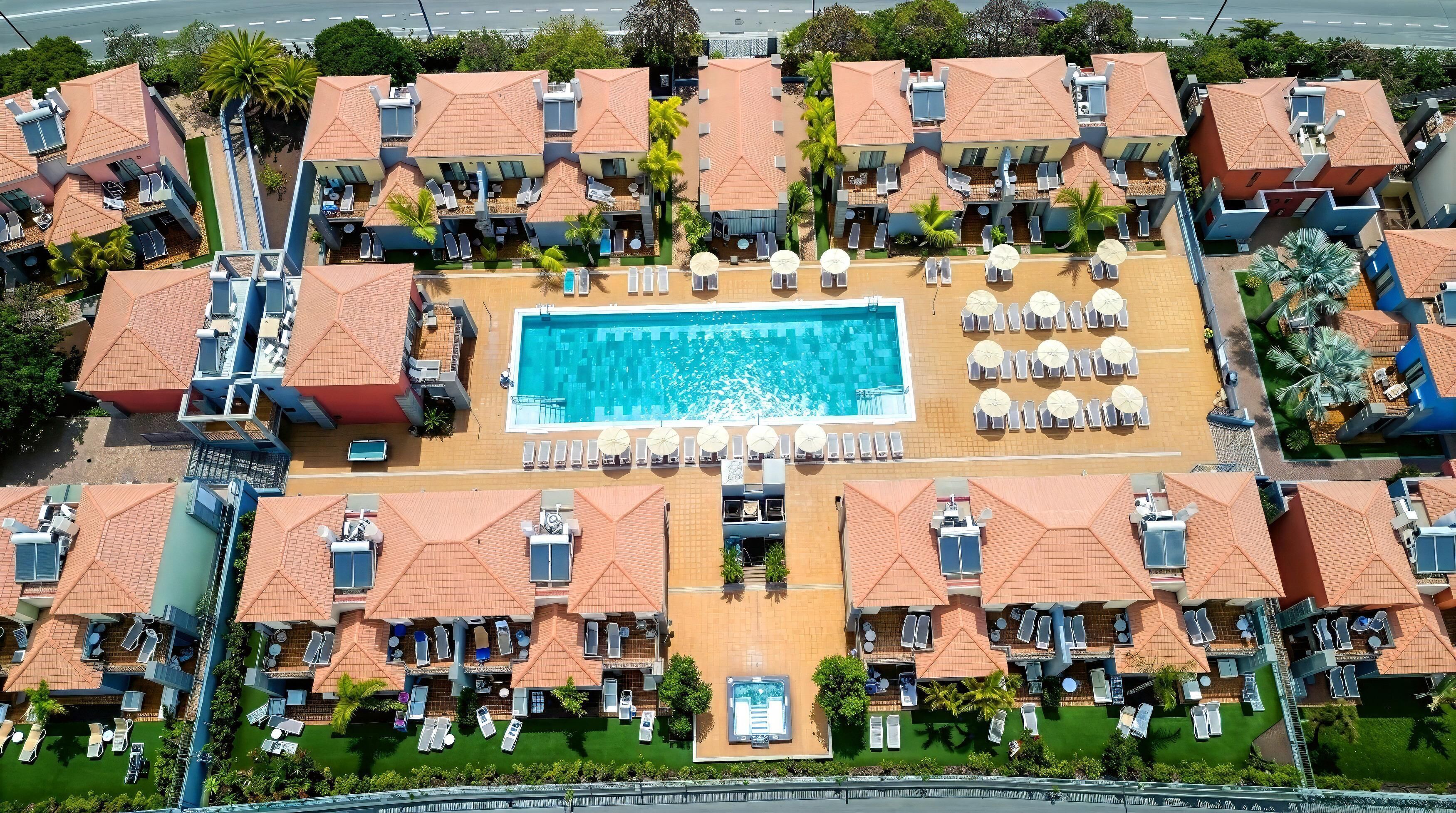 Vista aérea de un resort con varias edificaciones, una piscina central y tumbonas.