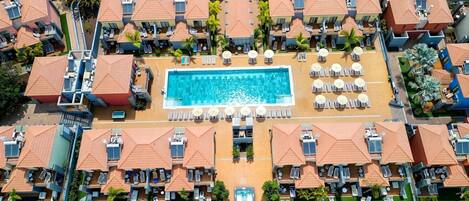 Vista aérea de un resort con varias edificaciones, una piscina central y tumbonas.