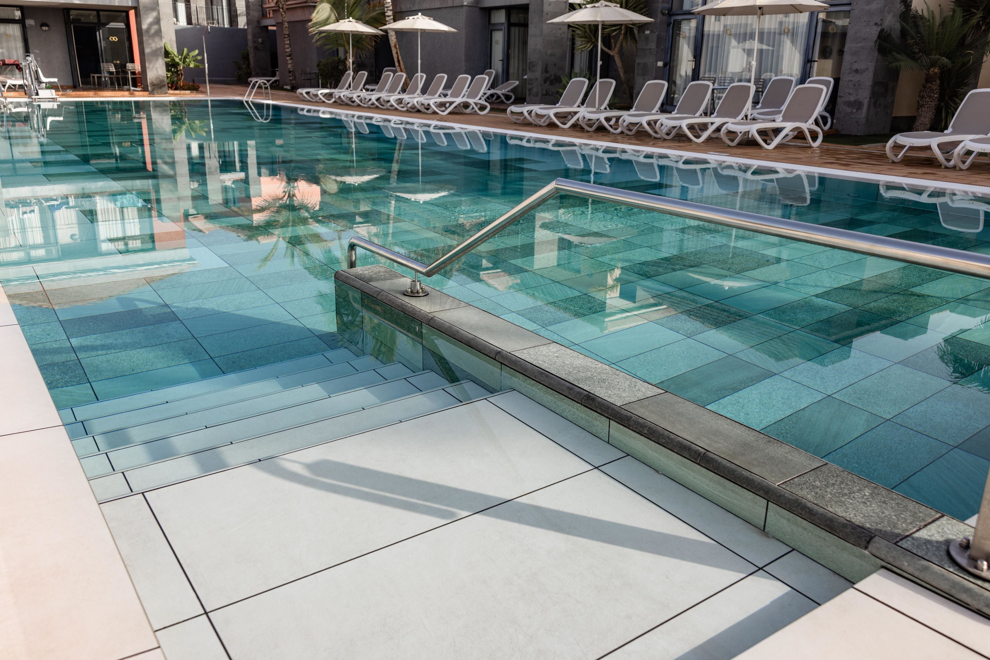 A swimming pool with clear water, tiled deck, and sun loungers.