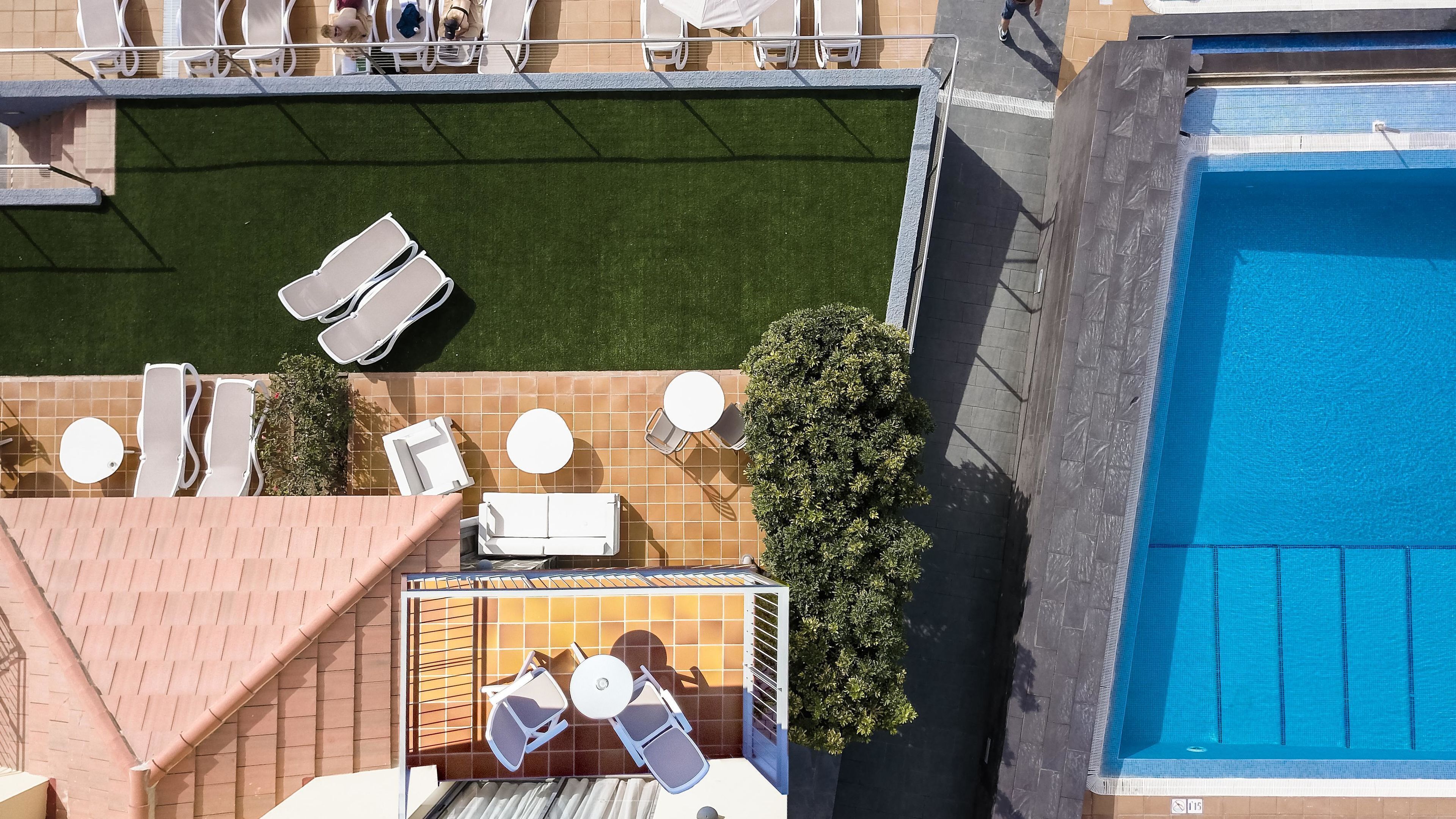 An aerial view of a rooftop pool area with multiple lounge chairs, a small table, and a large swimming pool.