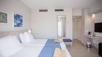 A hotel room with two beds, a blue towel, a TV, and a small table with a trash bin.