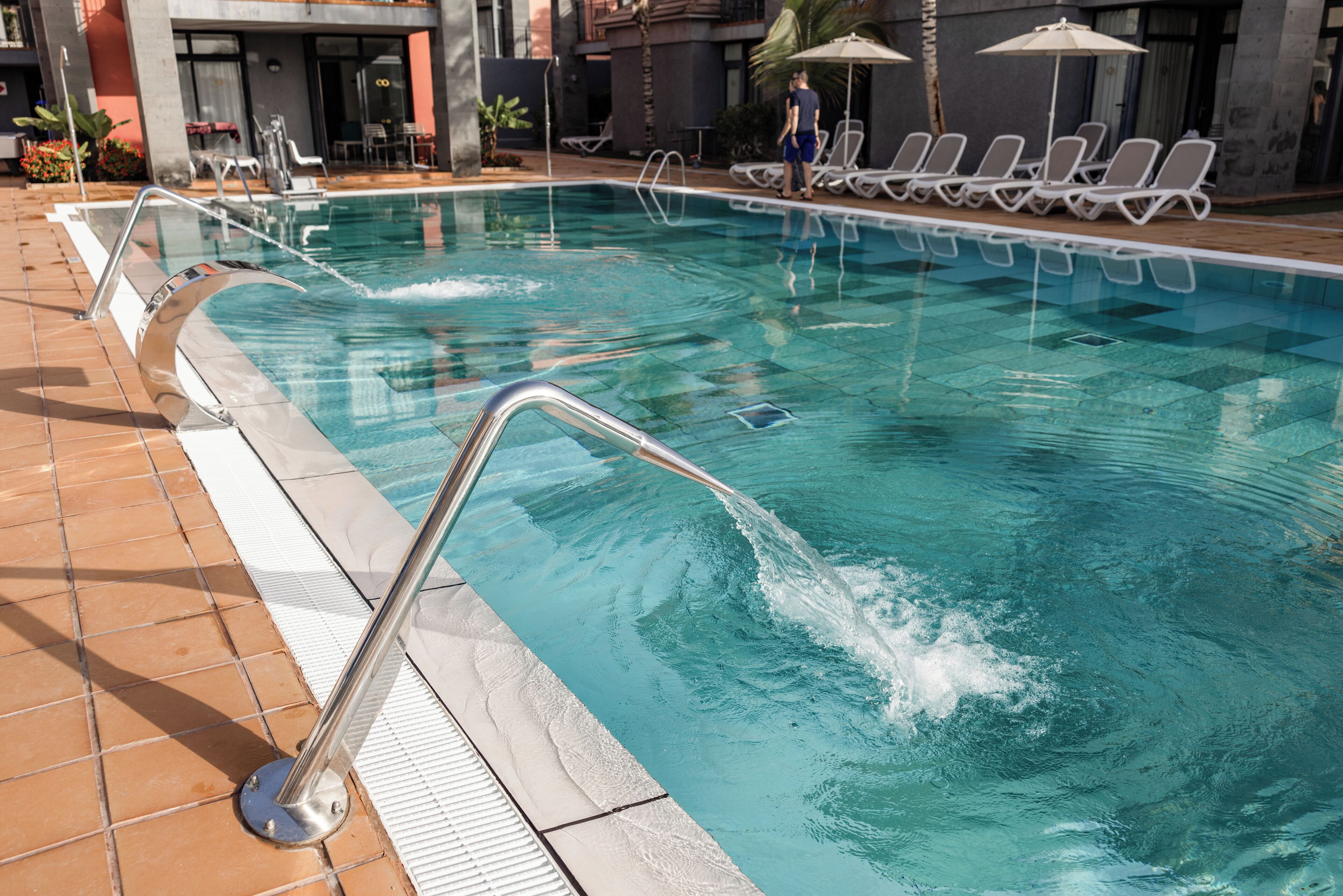 A swimming pool with a metal ladder, tiled floor, and lounge chairs around the perimeter.