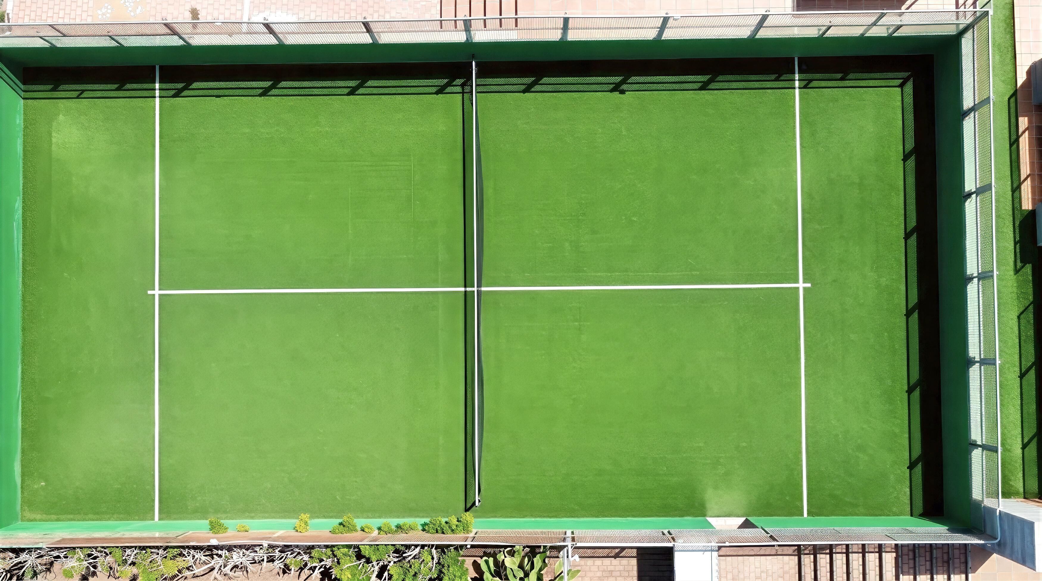 A tennis court with a net, surrounded by a green fence and a building with a brick facade.