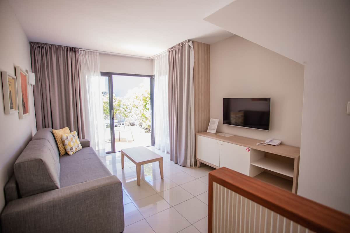 A modern living room with a sofa, a coffee table, a TV, and a sliding glass door leading to an outdoor area.