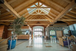 Eine großzügige Lobby mit hoher Holzbalkendecke, einem Empfangstresen, einer Steinwand und einem großen Rundbogenportal.