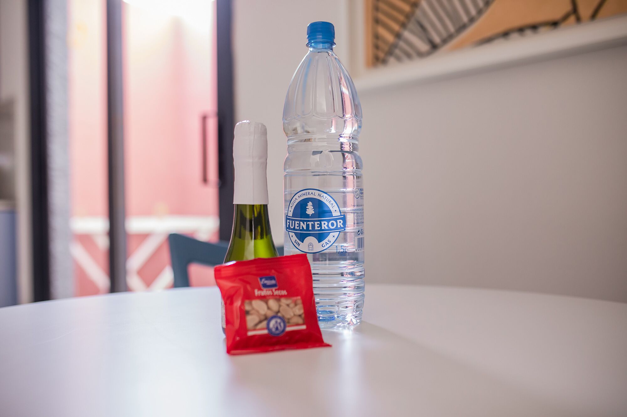 A bottle of FUENTEROR natural mineral water, a bottle of green wine, and a packet of almonds on a white table.