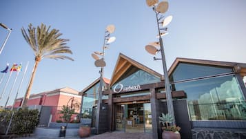 Un edifici modern amb façana de vidre, una palmera i antenes satèl·lit en pals.