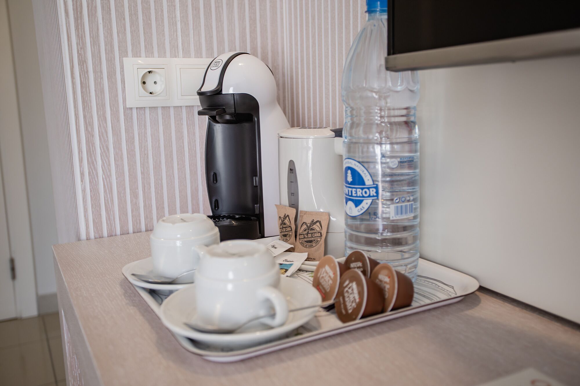 A breakfast tray with coffee maker, water bottle, cups, and coffee pods on a hotel counter.