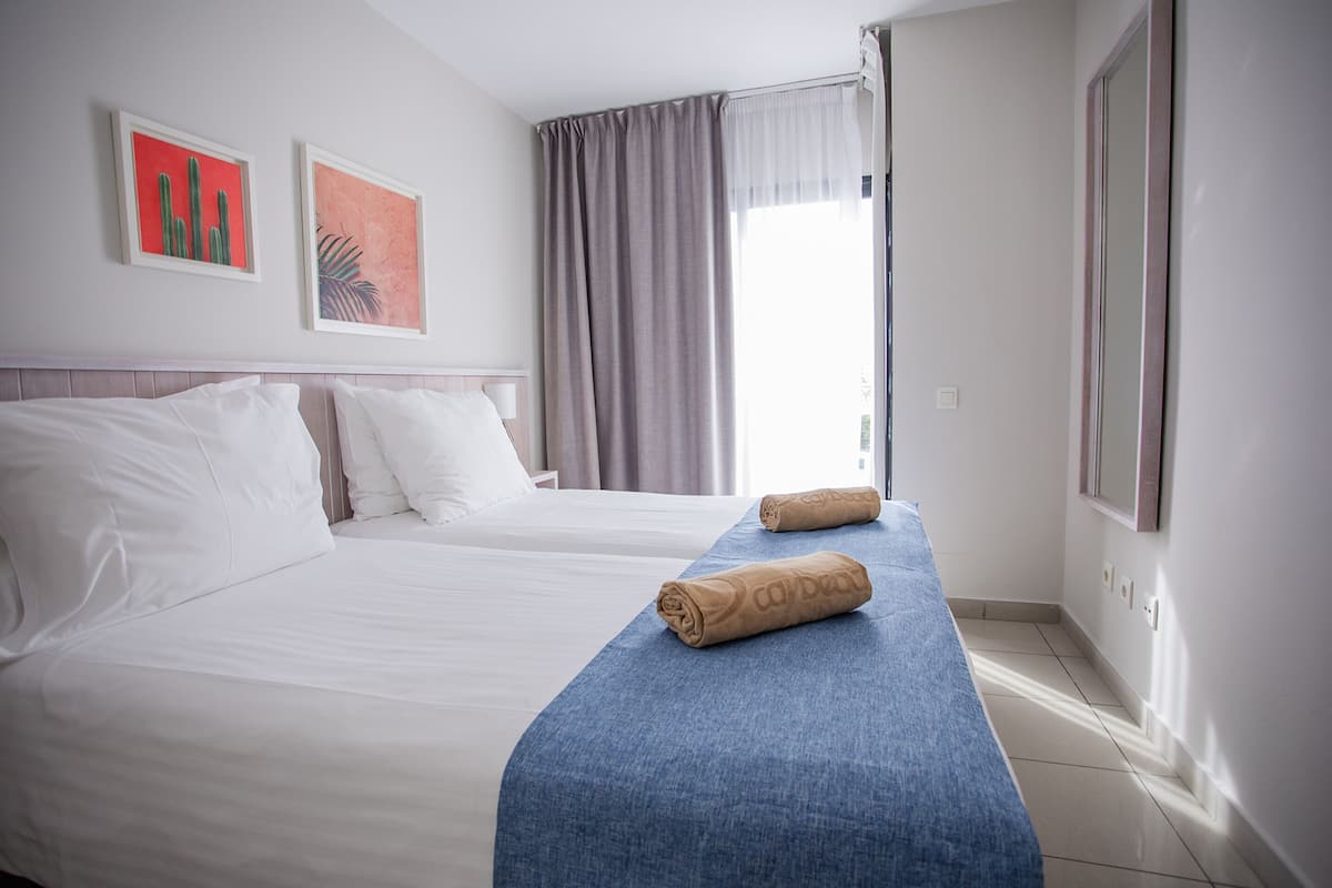 A hotel room with two beds, a blue bed runner, and artwork on the wall.