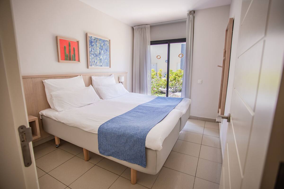 A hotel room with a bed, a nightstand, a window with curtains, and artwork on the wall.