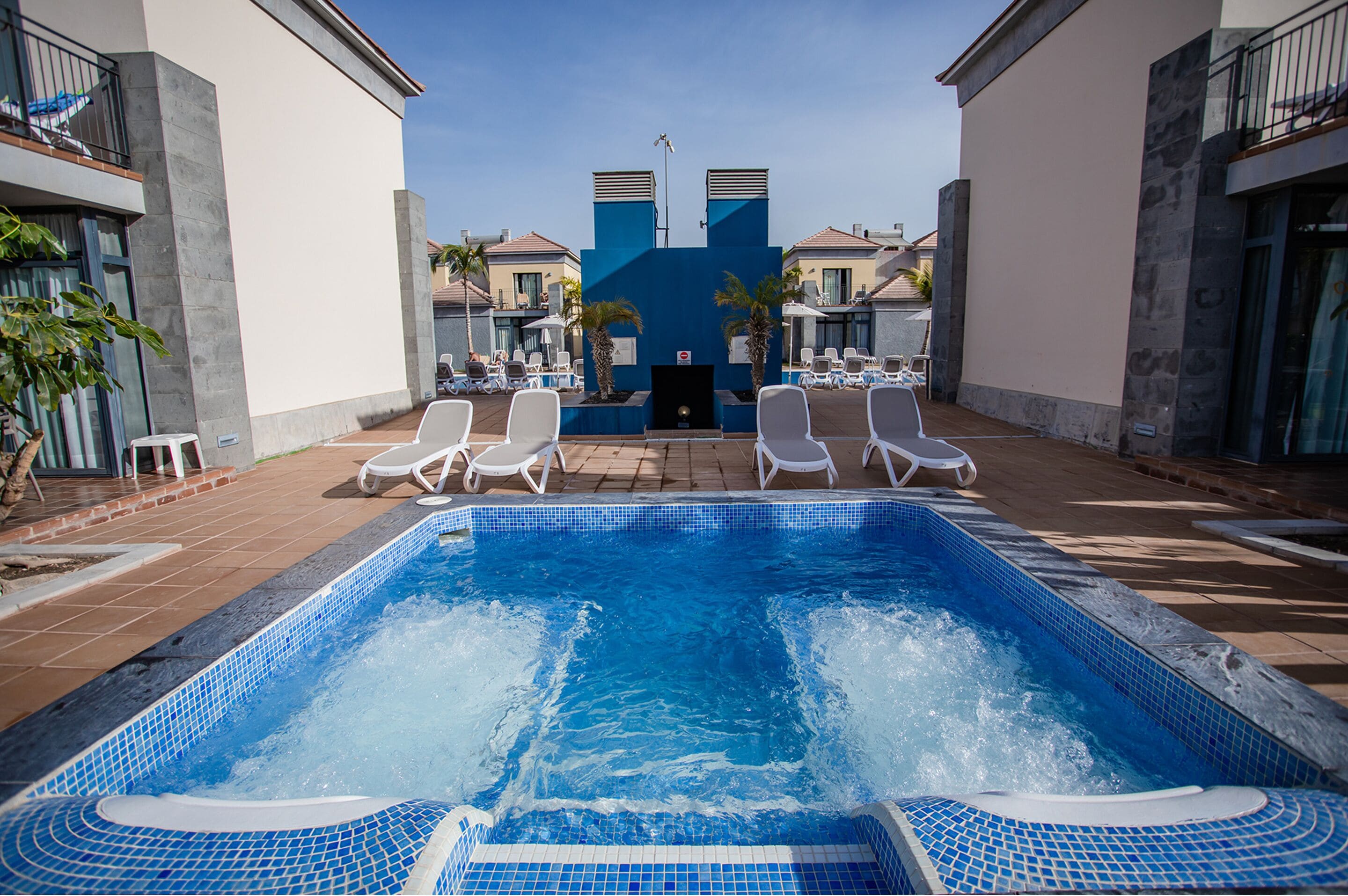 Une piscine avec des chaises longues, un jacuzzi et une vue sur un immeuble doté de balcons.