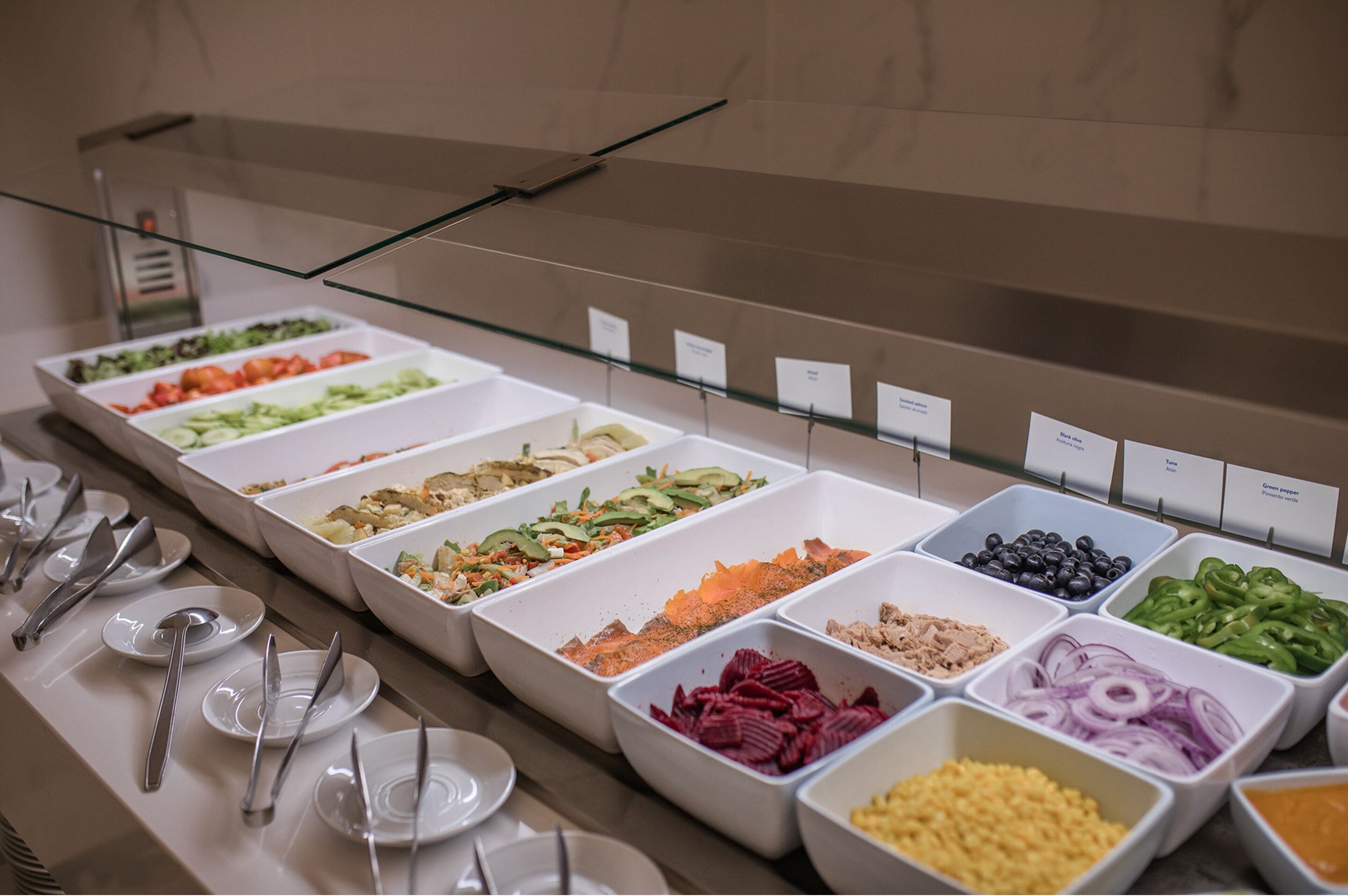 A buffet with various food items in white trays, each labeled with a name.