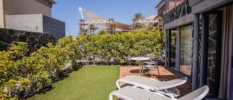 A patio with two white lounge chairs, a small table, and a stone wall.