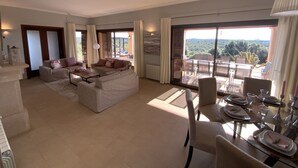 A spacious living area with a sofa set, a dining table set for four, and a large sliding glass door leading to an outdoor patio.