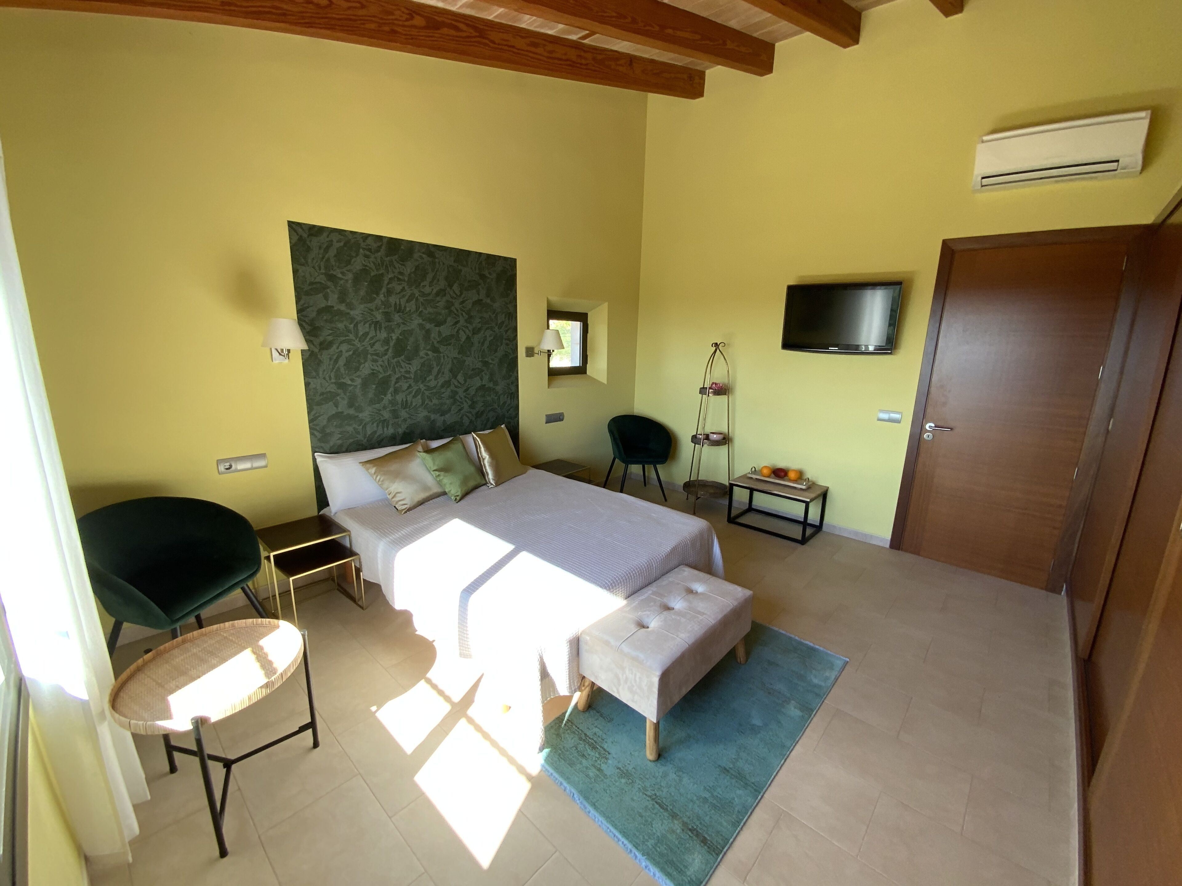 A bedroom with a bed, bedside tables, a chair, a TV, and an air conditioning unit.