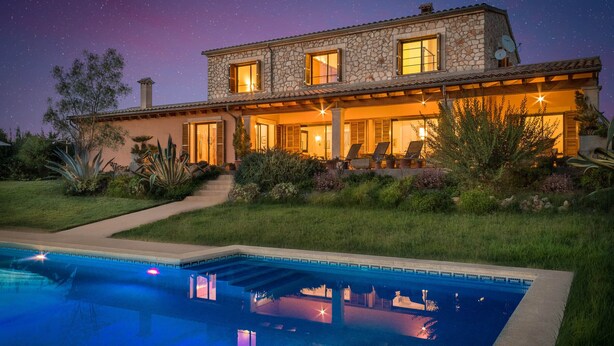 A two-story stone house with a swimming pool, outdoor seating, and a starry night sky.