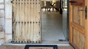 A wooden door with a rustic design, leading to an interior space with a dining area and a view of the outdoors.
