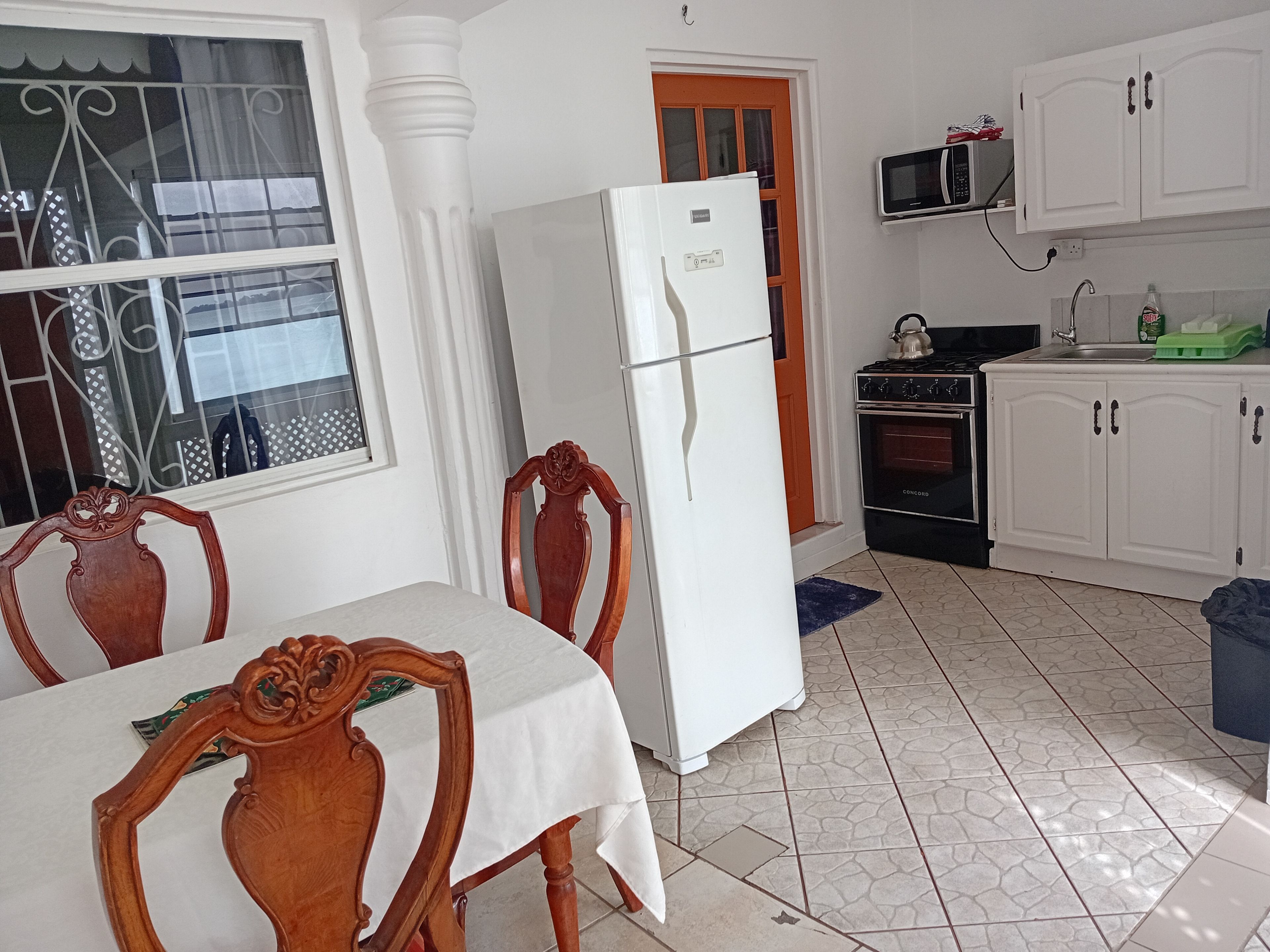 Een keuken met witte kasten, een koelkast, een fornuis en een eethoek met een tafel en stoelen.