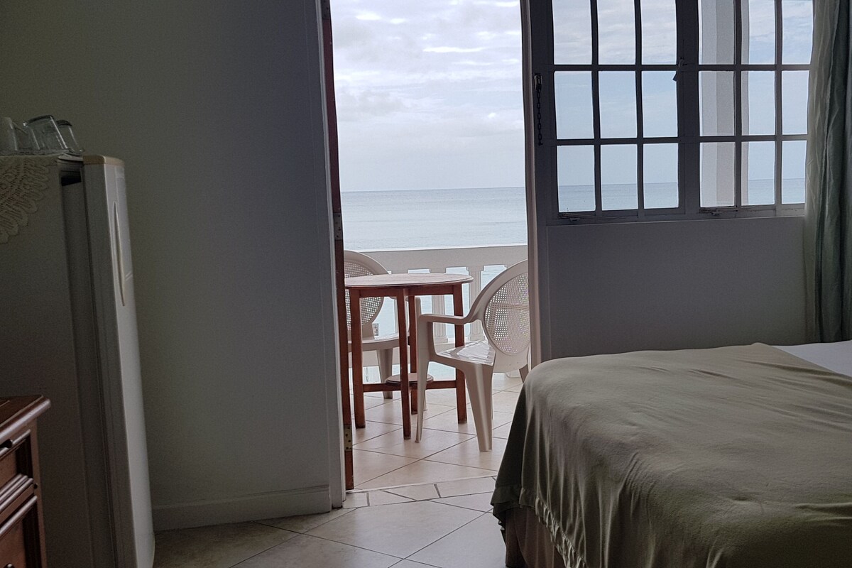 A hotel room with a bed, a small table, and chairs near a window with a view of the sea.