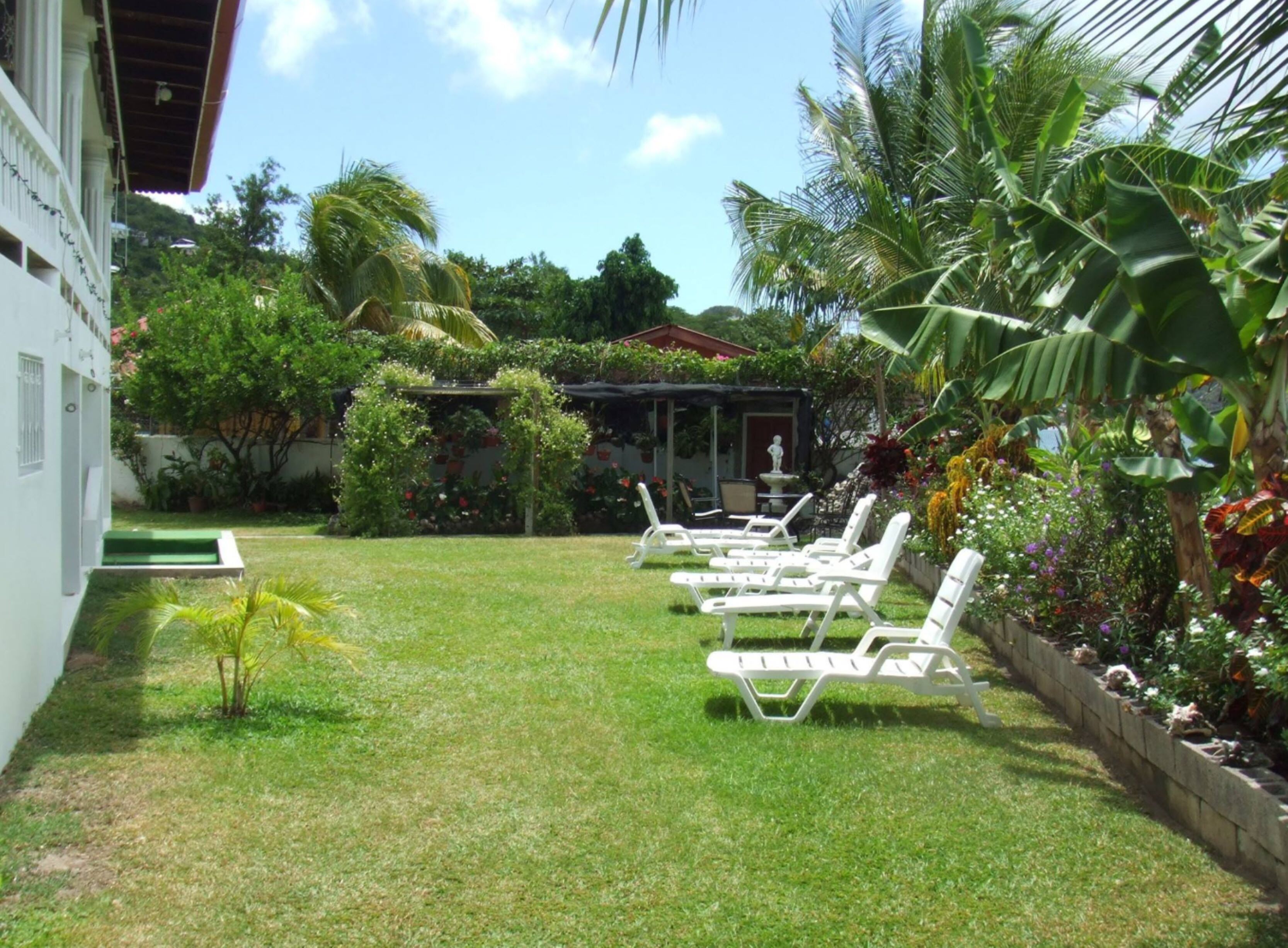 Un jardin avec une pelouse, des chaises longues blanches et une petite statue.