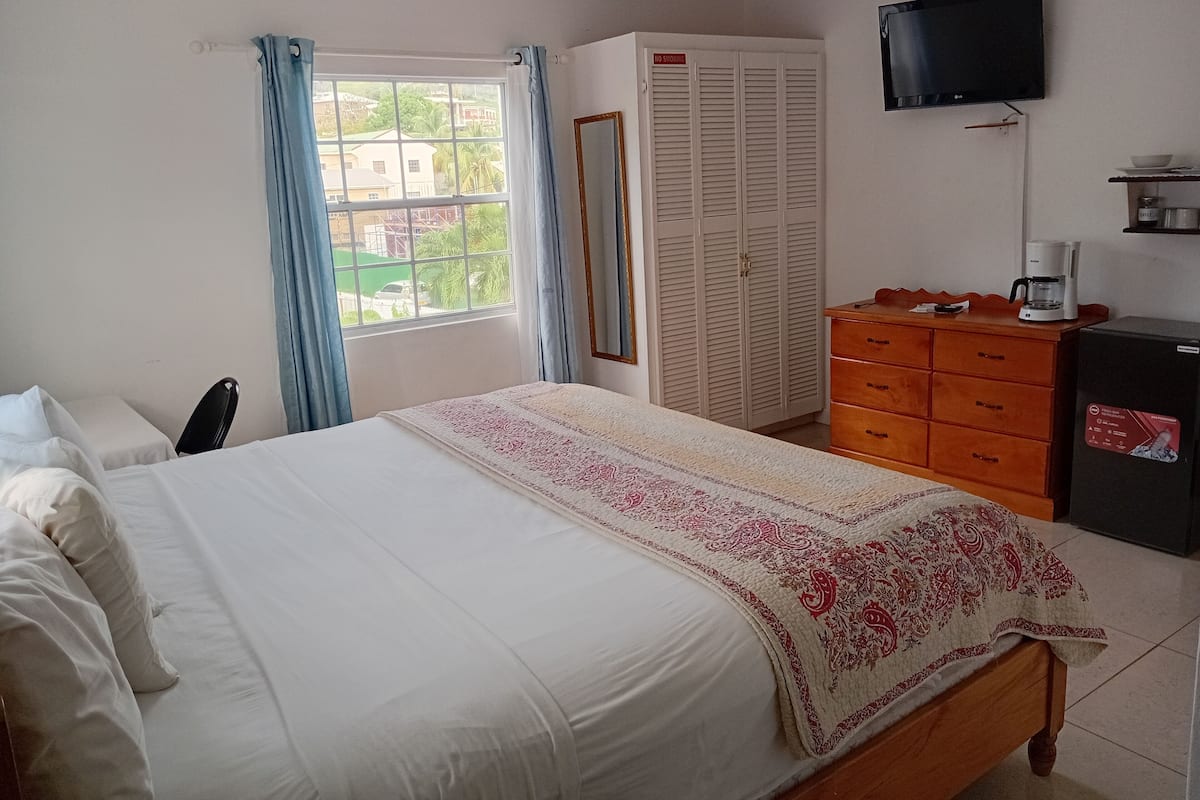 A hotel room with a bed, a wardrobe, a television, a coffee machine, and a window with curtains.