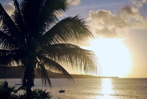 A sunset over a calm sea with a boat and palm trees. - Grand Anse Beach Palace (St. George's)