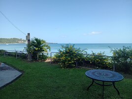 Un espacio al aire libre con césped, una mesa de metal y vistas al mar.