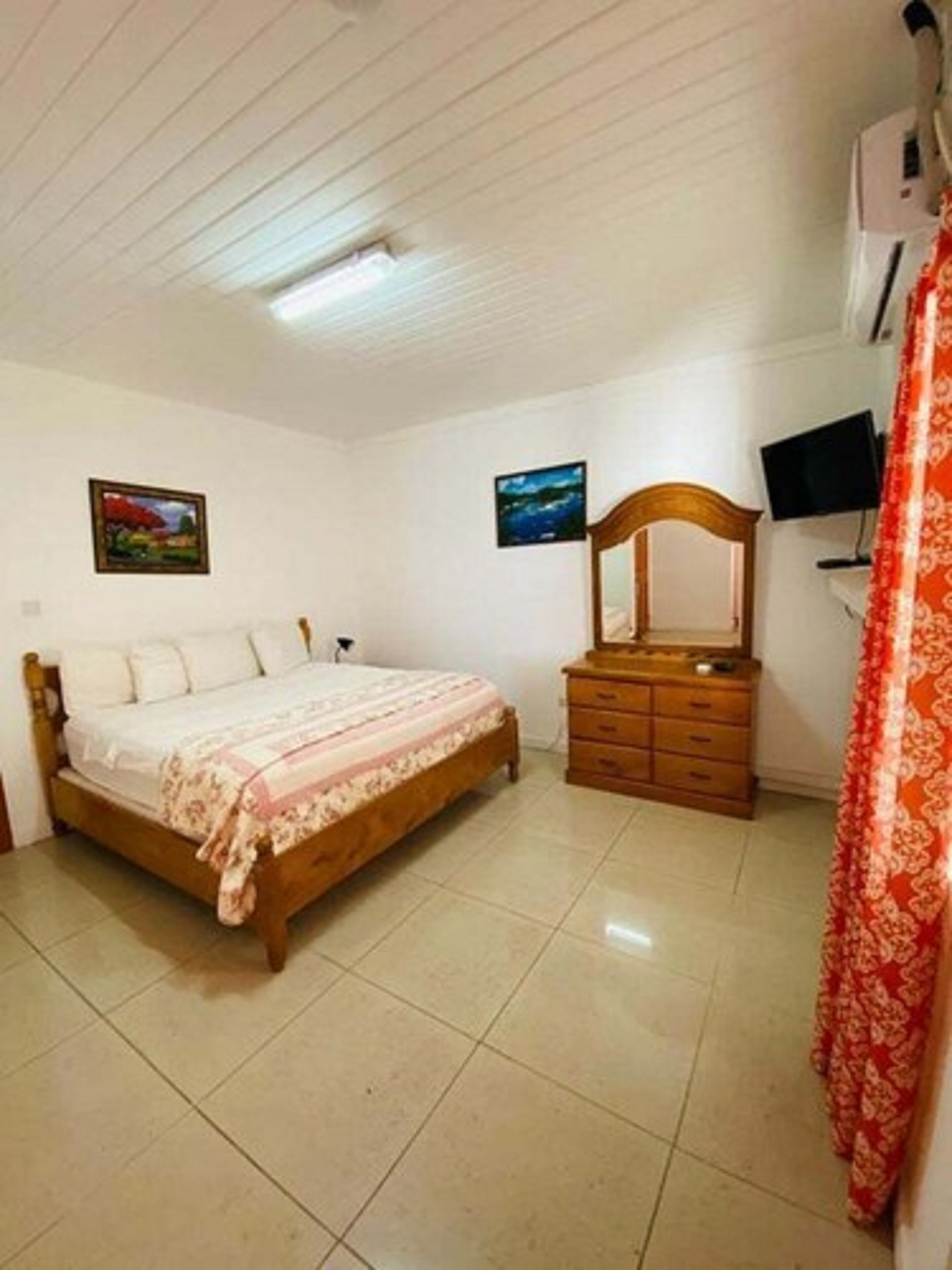 A bedroom with a bed, dresser, TV, and two paintings on the wall.