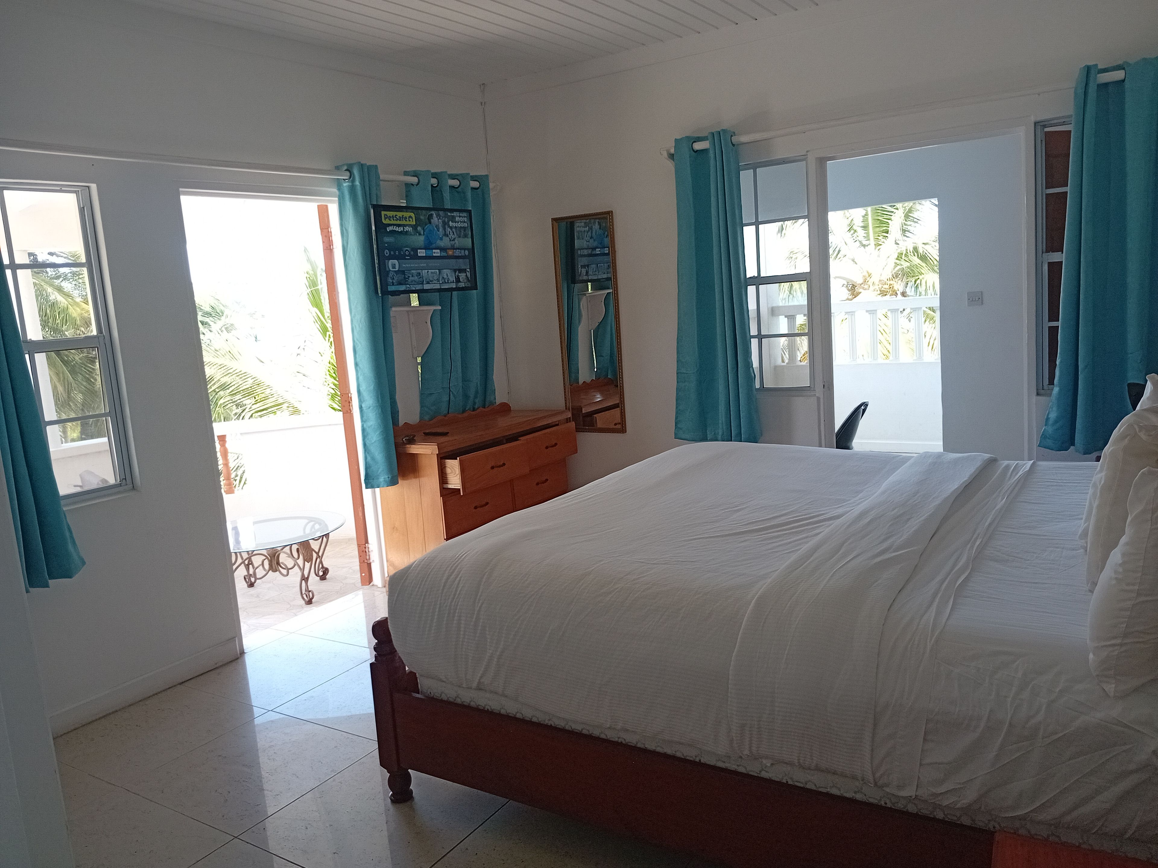 Une chambre à coucher avec un lit, une commode en bois, un miroir et une fenêtre avec des rideaux.