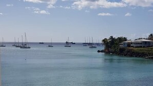 Una marina con varios veleros anclados en aguas tranquilas, cielo despejado y un edificio blanco a la derecha.