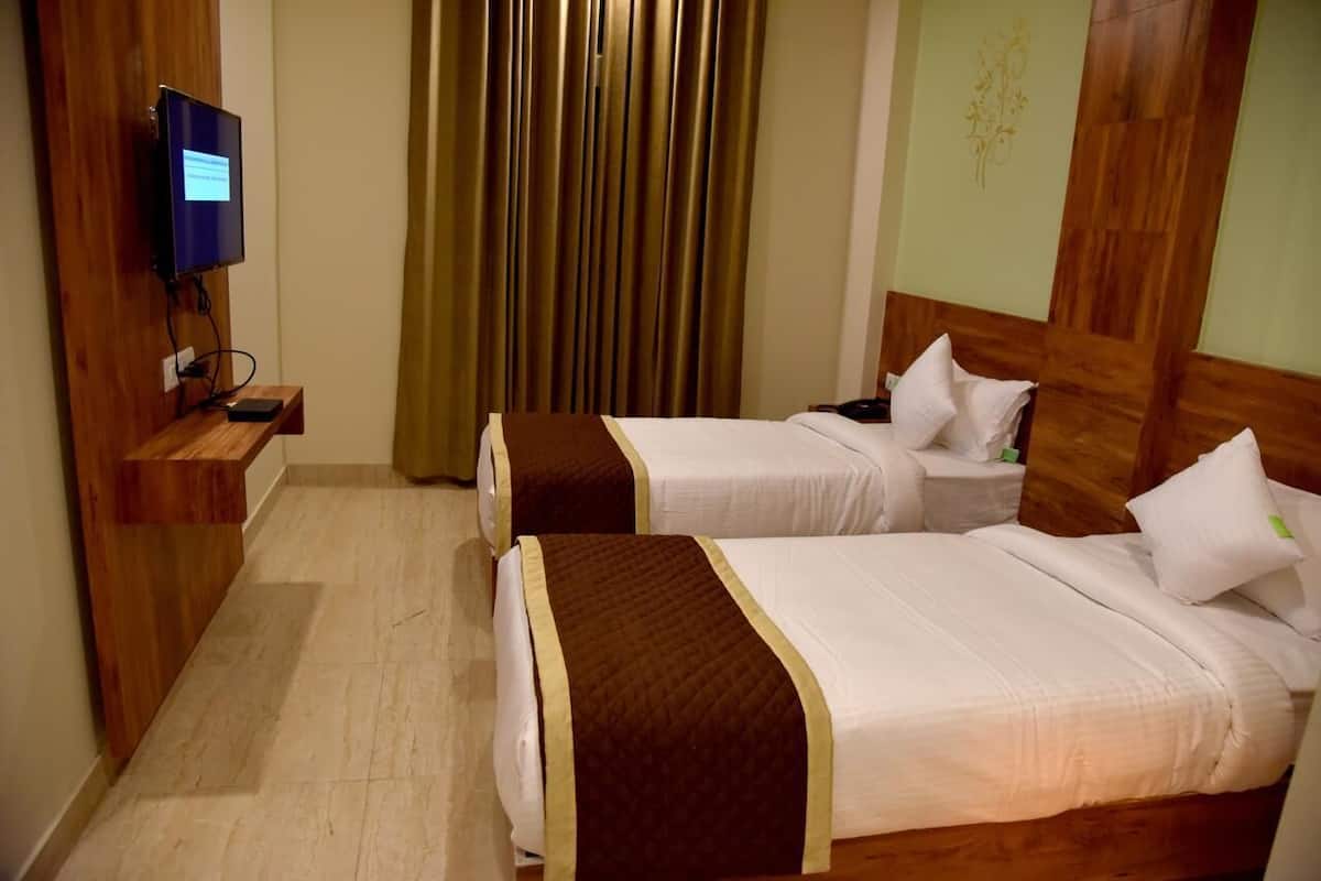 Een hotelkamer met twee bedden, een aan de muur bevestigde televisie en een houten hoofdbord.