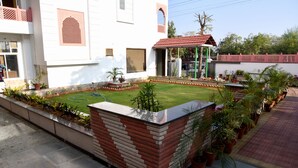 A residential area with a well-maintained lawn, a brick planter, and potted plants. - Hotel Triveni Residency Near SMS Stadium (Jaipur)